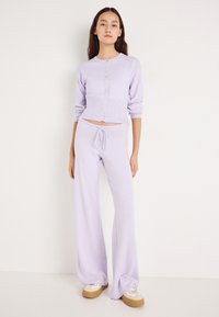 Σετ πλεκτών σε λιλά απόχρωση που περιλαμβάνει μια cropped ζακέτα με κουμπιά και ψηλόμεσα, άνετα παντελόνια με ρυθμιζόμενο κορδόνι στη μέση. Μαλακή υφή.