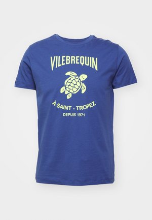 Sininen puuvillainen t-paita, jossa keltainen kilpikonnakuvio ja teksti "VILEBREQUIN À SAINT-TROPEZ DEPUIS 1971" klassisella fontilla. Pyöreä kaulus.