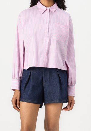 Femme portant une chemise à boutons rayée rose clair et blanche avec manches longues et un short taille haute bleu foncé.