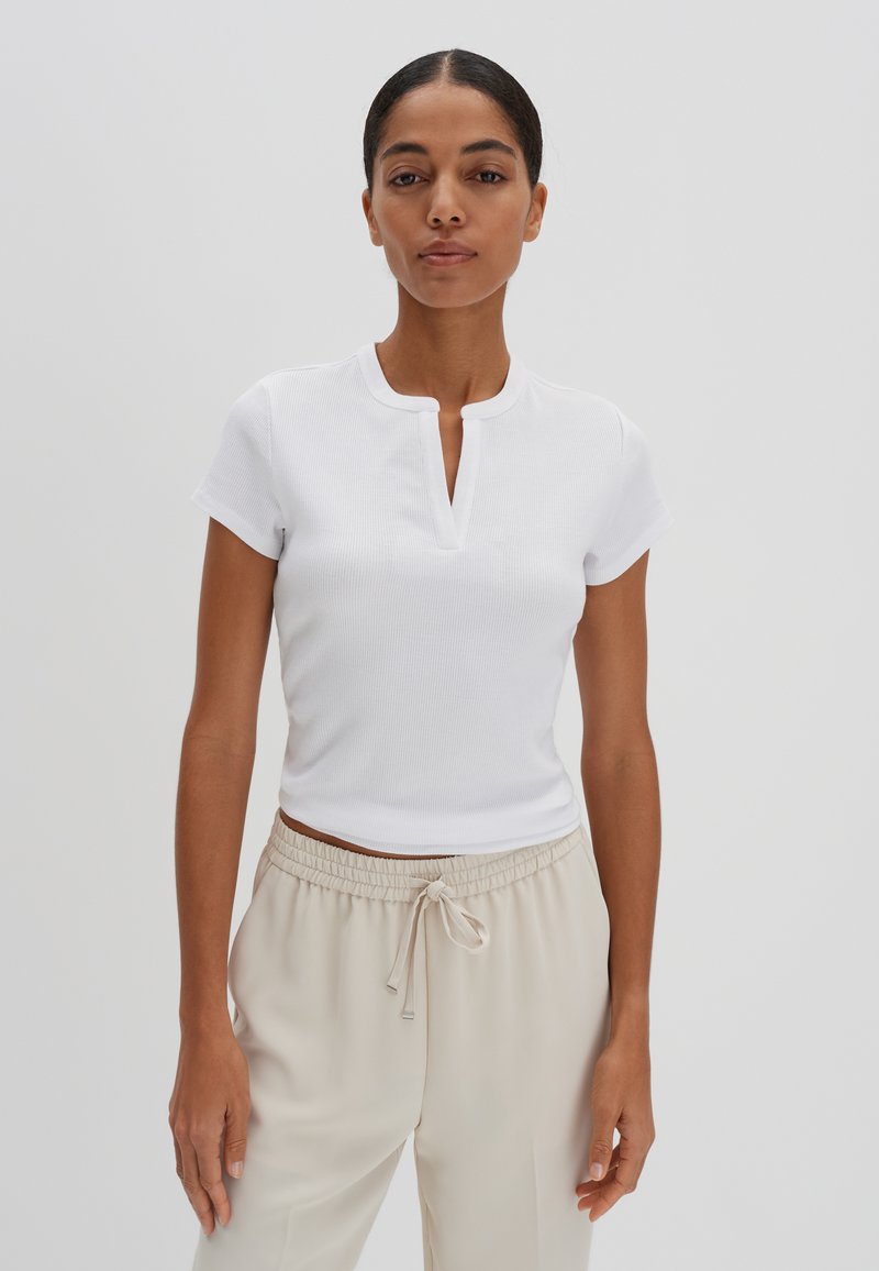 Witte geribbelde top met korte mouwen, een smalle knoopsluiting en een ontspannen pasvorm, gecombineerd met beige jogpants met trekkoord. Glad textuur, casual ontwerp.