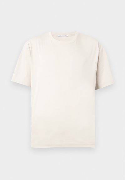 Απλή μπεζ κοντομάνικη μπλούζα με στρογγυλή λαιμόκοψη, απλωμένη επίπεδα σε ανοιχτό φόντο, χωρίς ορατά σχέδια ή γραφικά.