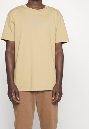 Beige Baumwoll-T-Shirt mit kurzen Ärmeln und Rundhalsausschnitt. Mit einem einfachen, in Hellblau gestickten Logo auf der linken Brustseite.