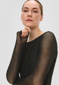 Czarny, przezroczysty top z długim rękawem o gładkiej fakturze, z szerokim dekoltem i przezroczystym materiałem. Rękawy delikatnie zwężają się w nadgarstkach.
