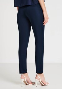 Pantalon ajusté bleu marine en tissu lisse au design épuré. Doté d'une poche arrière et assorti à des sandales à talons blancs.