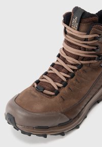 Brąsowe, wysokie buty wędrowne z beżowymi sznurowadłami, wyściełanym kołnierzem wokół kostki, teksturowaną podeszwą i logo "The North Face" na języku.