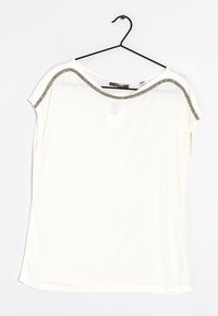 Camiseta blanca de manga corta con un corte relajado, que presenta un escote con acentos metálicos y una tela suave y ligera. Cuélga de un gancho negro.