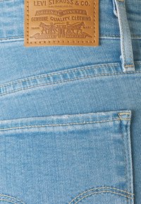 Écusson en cuir marron Levi Strauss & Co. sur un jean en denim bleu clair avec coutures visibles et détail de la poche arrière.
