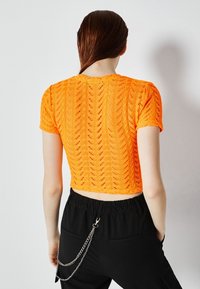 Virkatusta kirjavankeltaisesta crop-topista, jossa on teksturoitu sahalaitakuvio. Lyhyet hihat, takaosasta näkyy siisti viimeistely ja resorireunat.
