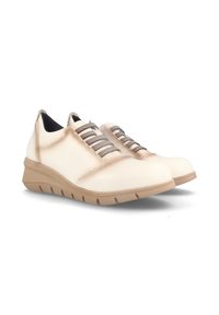 Zapatos de cuero beige con suela de goma, que cuentan con cordones elásticos en zigzag y un diseño de puntera redondeada, ofreciendo una apariencia casual pero moderna.