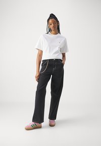 Sorte høyt liv jeans med en kjededetalj, kombinert med en hvit bomull t-skjorte og rosa sneakers med grønne striper.