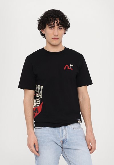 T-shirt en coton noir avec un petit motif rouge sur la poitrine et un grand design coloré sur le côté. Manches courtes et coupe classique.
