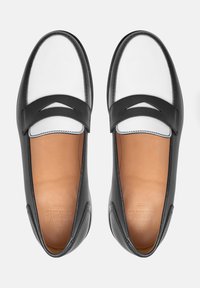 Zwarte leren instappers met een witte neus, voorzien van een decoratieve uitsnijding en contrasterende stiksels. Soepele binnenvoering.