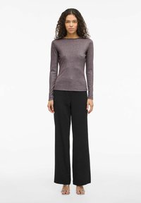 Top de manga larga metalizado en color púrpura con cuello redondo, combinado con pantalones anchos negros y sandalias minimalistas de tira transparente.