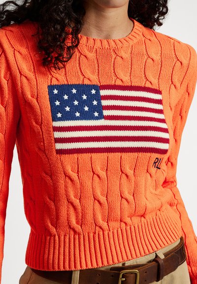 Kötött pulóver élénk narancssárga színben, amely amerikai zászló mintával van díszítve, kék, fehér és piros csíkokkal. Bordázott szegély és mandzsetták.