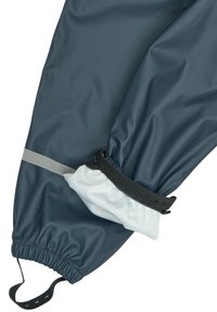 Ropa exterior impermeable azul oscuro con puños elásticos; detalle de tira gris; forro blanco suave visible en el puño, mostrando un diseño en capas.