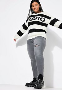 Suéter de rayas en blanco y negro con textura de punto y logo, combinado con jeans grises desgastados y zapatos de plataforma negros.