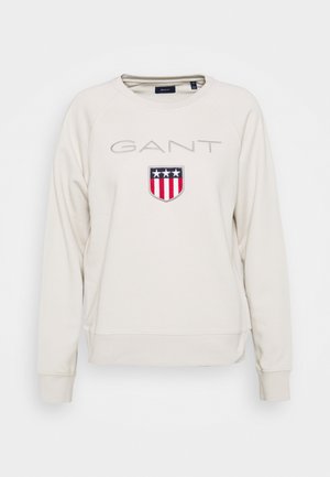 Cremeweißer Sweatshirt mit Rundhalsausschnitt, "GANT" Schriftzug und Schild-Emblem mit drei weißen Sternen über roten und weißen Streifen auf der Brust.