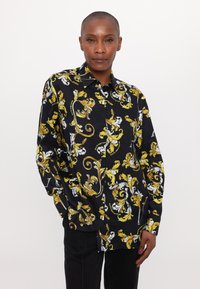 Camicia nera con intricati motivi floreali gialli e bianchi, progettata con colletto e maniche lunghe.