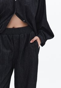 Mörk denimskjorta med avslappnad passform, med knappstängning och uppvikta ärmar. Matchas med byxor med elastisk midja.