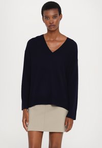 Marineblå v-hals genser laget av myk, teksturert stoff, med lange ermer og en litt cropped søm, sammen med en lys beige skjørt.