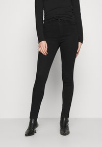 Černé úzké džíny vyrobené z denimu s klasickým designem pěti kapes, slim fit a jemným zesvětlením na kolenou, doplněné černými botami na podpatku.