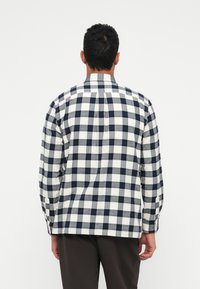 Langwerpige, geruite blouse met een blauw-wit patroon, gemaakt van een zachte stof met een kraag en knoopmanchetten.