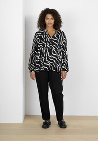 Chemise à motifs noir et blanc avec des manches longues, un col et des détails de boutons, assortie à un pantalon noir et des chaussures noires épaisses.