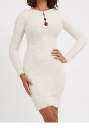 Kobieta ubrana w długą, białą, puszystą dzianinową sukienkę z długim rękawem, z trzema małymi wycięciami z przodu w okolicy dekoltu oraz ściągaczem na dole.
