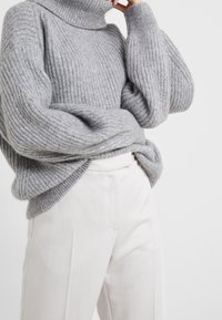 Harmaa neulottu pooloneule, jossa on resorikuvio ja ylisuuria hihoja, yhdistetty vaaleisiin beigen sävyisiin housuihin.