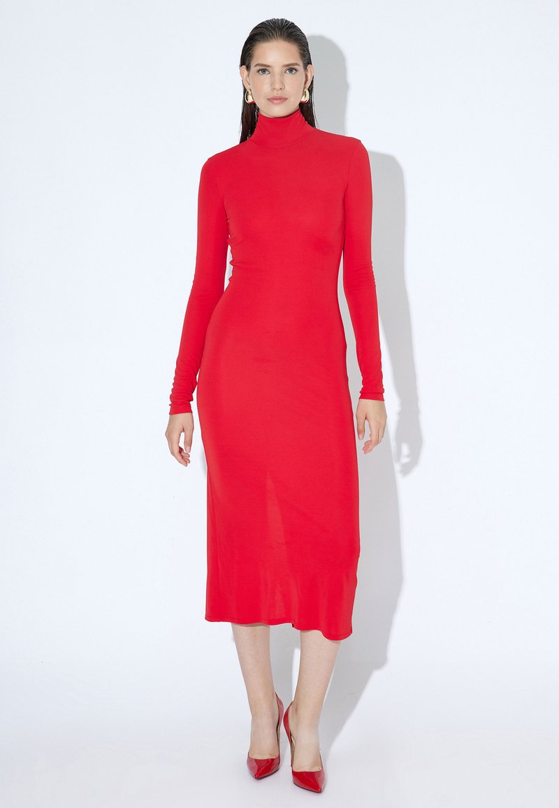 Rød, langærmet, turtleneck kjole i slim fit, med midi længde og glat tekstur. Båret med matchende røde spidse hæle.
