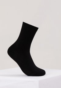 Calzino di cotone nero con orlo a costine, alla caviglia, texture liscia e punta arrotondata. Posizionato in verticale su una superficie bianca.