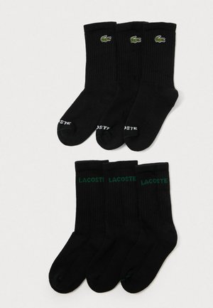 Drei Paare schwarze Crew-Socken mit grünen Lacoste-Logos und drei Paare mit weißen Lacoste-Logos, angeordnet auf einem weißen Hintergrund.
