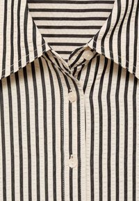 Gros plan d'une chemise à rayures verticales noires et blanches avec col et boutons blancs sur le devant.