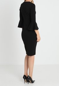 Černé přiléhavé šaty s tříčtvrtečními zvonovými rukávy, vyrobené z hladké látky. Mají zadní zip a délku ke kolenům. Spárovány s černými podpatky.