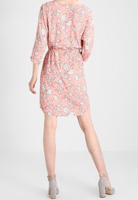 Lilarosa blommig klänning med trekvartslånga ärmar, ett elastiskt midjeband och en flödande design. Tyget har en slät textur med vita blommönster.