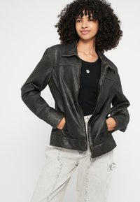 Črna usnjena jakna z zadrgo spredaj, z zarezanim ovratnikom in dvema stranskima žepoma. Nosi se čez črno majico in svetlo sive raztrgane kavbojke.