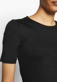Camisa negra de manga corta con escote redondo, textura suave y diseño ajustado. Los detalles de costura son visibles en las mangas.