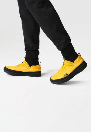 Baskets jaunes avec une tige lisse et une semelle en caoutchouc noire. Comprend un bout arrondi, un système de laçage et un logo sur le côté.