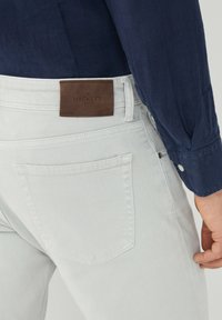 Jeans de mezclilla gris claro con un parche de piel del logo de Hackett en la parte trasera, que presenta un diseño clásico de cinco bolsillos y detalles de costura sutiles.