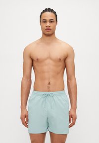 Shorts de bain bleu clair en matériau léger, dotés d'une taille élastique avec cordon de serrage et de poches latérales.