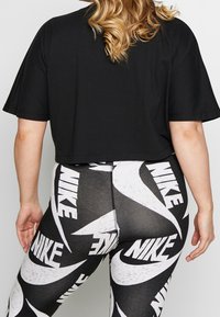 Svart kortärmad cropped t-shirt som matchas med svarta leggings med stora vita "Nike"-logotyper och ett strukturerat mönster.
