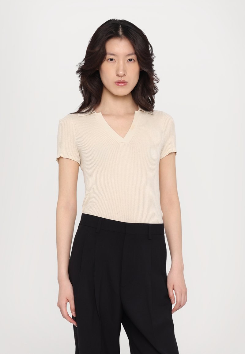 Beige ribbed v-neck top with short sleeves paired with black tailored trousers. Smooth texture, fitted design, and subtle collar detail.