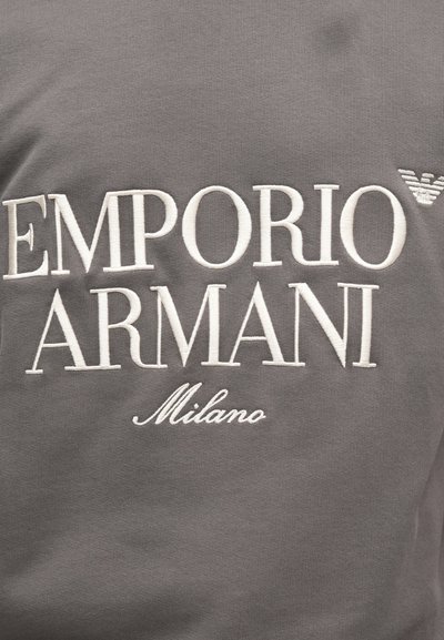 Sivá mikina s bielym vyšitým textom "EMPORIO ARMANI" a "Milano" a malým logom orla v pravom hornom rohu.