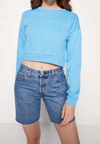 Light blue cropped sweatshirt with long sleeves, paired with high-waisted blue denim shorts featuring frayed hems and a classic five-pocket design.