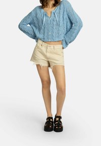 Světle modrý pletený krátký kardigan se zapínáním na knoflíky a stahovací šňůrkou, kombinovaný s béžovými roztrhanými džínovými šortkami. Nosit s černými sandály na platformě se šňůrkami.
