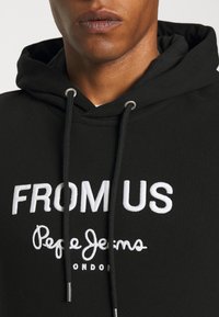 Felpa nera con cappuccio caratterizzata da testo ricamato in bianco "FROM US" e "Pepe Jeans LONDON." Include lacci e dettagli in metallo. Tessuto morbido.