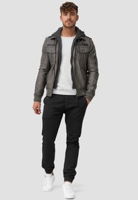 Chaqueta de cuero gris con capucha, suéter gris debajo, pantalones negros y zapatillas blancas. Diseño simple con cremallera y detalles de bolsillo.