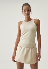 Light beige activewear set featuring a fitted sleeveless top and a flared skirt. Smooth texture with contrasting stitching and subtle logo detail.