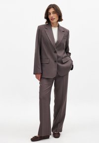 Gray blazer with two buttons, notch lapels, and front pockets, paired with matching gray trousers. Smooth fabric with a tailored fit.