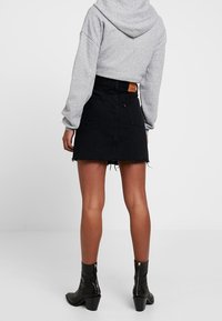 Jupe en denim noir avec ourlet effiloché, taille haute et poche arrière. Associée à un sweat à capuche gris et des bottines noires avec un détail de fermeture éclair.